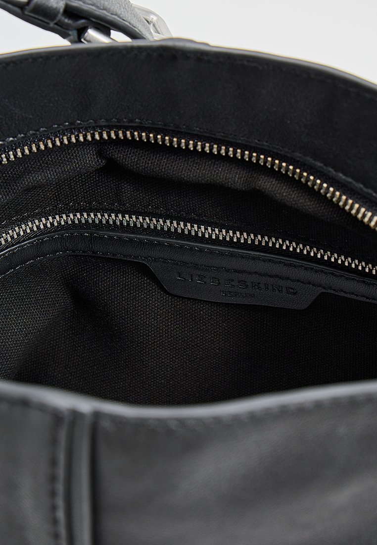 Innenansicht einer schwarzen Lederhandtasche mit glatter Textur, ausgestattet mit einem kontrastierenden Stofffutter und einer Reißverschlusstasche. Markenetikett sichtbar im Inneren.