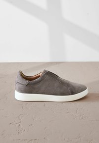 Gray suede slip-on shoe with textured surface, elastic side accents, and a white rubber sole. Minimalist design, suitable for casual wear.