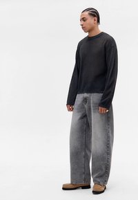 Czarny sweter z siateczki z długim rękawem o luźnym kroju, w połączeniu z luźnymi szarymi dżinsami i beżowymi butami wsuwanymi. Subtelna faktura i detale designu.