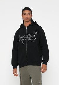 Čierna mikina na zips s predným klokankovým vreckom, so bielym logom na hrudi. Vyrobená z mäkkého, textúrovaného materiálu.
