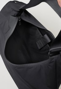 Borsa in tessuto nero con apertura a cerniera. L'interno presenta una texture liscia e un attacco per una tracolla. Cerniera robusta e manici resistenti.