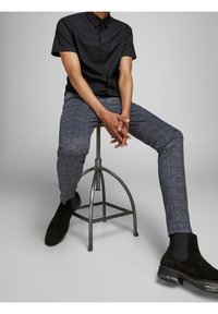 Černá košile s krátkým rukávem na knoflíky v kombinaci s kostkovanými slim-fit kalhotami v odstínech modré a šedé, doplněná černými semišovými kotníkovými botami.