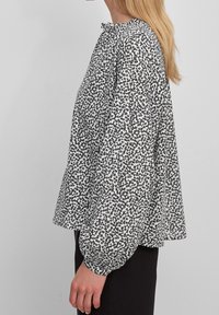 Zwart-wit gebloemde blouse met een ronde hals, opstaande lange mouwen en een relaxte pasvorm, gemaakt van lichtgewicht stof.