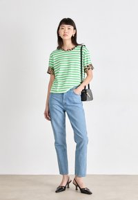 Groen en witte gestreepte T-shirt met luipaardprint manchetten, gecombineerd met lichtblauwe jeans en zwarte hakken. Kleine zwarte handtas.