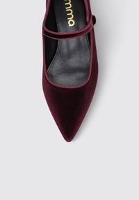 Zapato de estilo Mary Jane de terciopelo burdeos con punta afilada, que presenta un forro interior negro y una correa delgada cruzando el empeine.