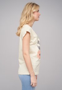 T-shirt à manches courtes jaune clair avec un motif floral ; en coton doux, coupe décontractée, col rond, associé à un jean bleu moulant.