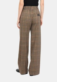 Pantaloni a gamba larga a quadri con motivo check marrone e beige. Presentano un elastico in vita e una tasca posteriore con dettaglio del marchio.