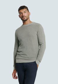 Lichtgrijze gebreide trui met textuur, lange mouwen, ronde halslijn en geribbelde boorden en zoom. Gepaard met donkere broek.
