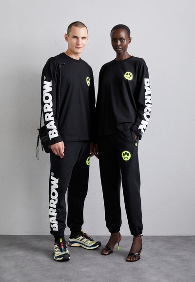 Black long-sleeve shirts and pants with neon smiley face designs. "BARROW" logo in white on sleeves and sides, paired with sporty sneakers.