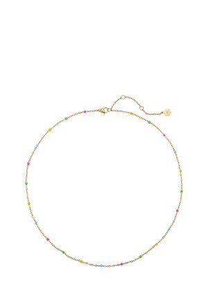 Woman wearing a white blazer and matching delicate gold necklace and bracelet with small colorful beads, hand resting on chest.