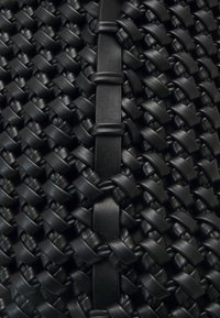 Czarny, pleciony materiał skórzany o tkanej fakturze, z płaskimi, skórzanymi akcentami rozmieszczonymi na całej powierzchni. Wzór jest skomplikowany i jednolity.