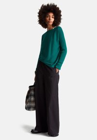 Miętowy prążkowany top z długim rękawem o luźnym kroju, zestawiony z luźnymi czarnymi spodniami. Torebka na ramię w czarno-białą kratę, błyszczące czarne buty.