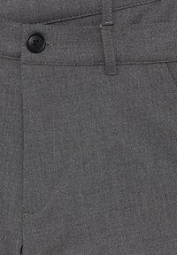 Tissu gris en gros plan d'un pantalon sur mesure avec un bouton noir, une passants de ceinture et des coutures visibles sur la poche avant.