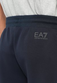 Jūras spēku sporta bikses ar elastīgu jostu, ar pelēku "EA7 Emporio Armani" logo. Gluda auduma tekstūra, šaura piegriezuma dizains.