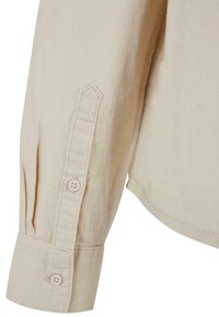 Poignet de chemise beige à manches longues avec deux boutons et détail patte de boutonnage cousue sur un tissu lisse.