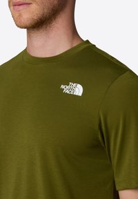 Olivově zelené tričko s krátkým rukávem vyrobené z hladkého materiálu, s bílým logem na levém rameni a kulatým výstřihem.