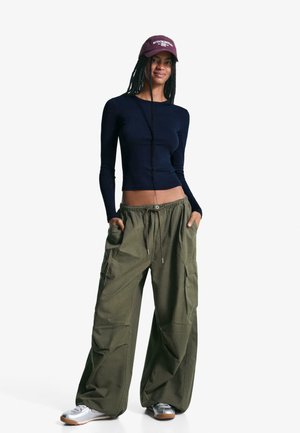 Bluză cu mânecă lungă, de culoare bleumarin, cu croială mulată și închidere cu nasturi, combinată cu pantaloni cargo largi, de culoare măslinie, cu buzunare laterale și talie elastică.