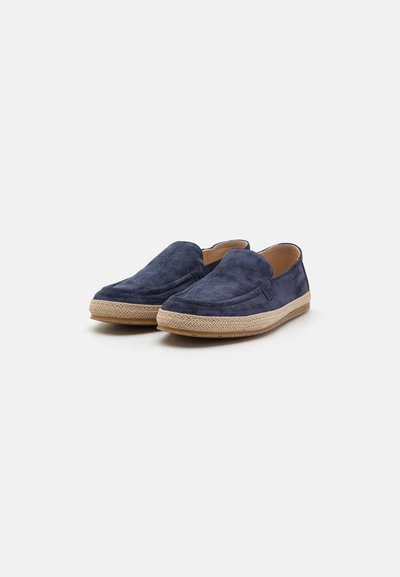 Chaussures slip-on en daim bleu marine avec un bout arrondi, semelle en jute de style espadrille et doublure lisse, présentant des détails de couture minimalistes.