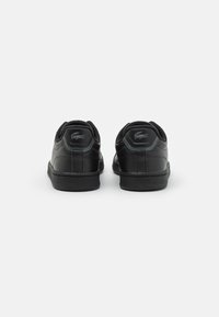 Baskets en cuir noir avec des accents en tissu noir texturé, un col rembourré, une semelle en caoutchouc et un logo bien visible à l'arrière.