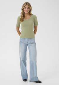 Top ribbed tricot verde deschis cu mâneci scurte și decolteu pătrat, asortat cu blugi largi de spălare deschisă și pantofi negri.
