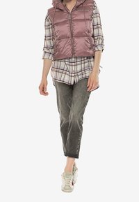 Růžová vycpaná vesta s kapucí over kostkovanou košilí, doplněná šedými džíny a krémovými teniskami. Obsahuje zip a nastavitelné stahování.