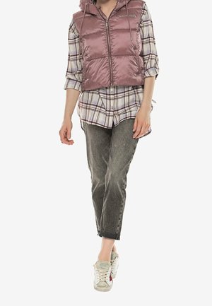 Vadderad rosa väst med huva över en rutmönstrad skjorta, kombinerad med grå jeans och krämfärgade sneakers. Har dragkedja och justerbar snörning.