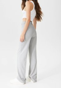 Lichtgrijze, hoge taille, wijde broek gemaakt van gestructureerde stof. Voorzien van zijzakken en een strakke, op maat gemaakte silhouet.