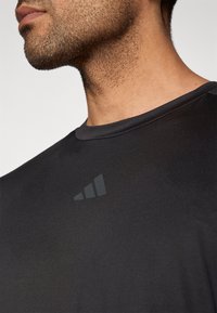 Μαύρο αθλητικό μπλουζάκι με στρογγυλή λαιμόκοψη και κοντά μανίκια. Διαθέτει υφασμάτινη υφή και διακριτικό σκούρο λογότυπο στο στήθος.