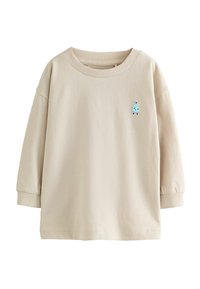 Beige långärmad skjorta med en liten blå broderad karaktär på bröstet. Skjortan har en avslappnad passform och ribbade ärmslut.