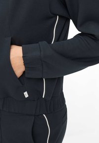 Marineblauer Sweatshirt mit weißen Akzentnähten, lockerem Schnitt, gerippten Bündchen und einer Seitentasche, gefertigt aus weichem Baumwollmischgewebe.