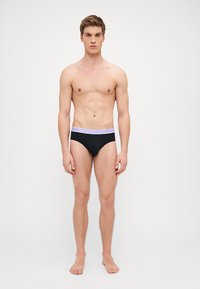 Brief neri con una fascia viola che presenta il logo 'Emporio Armani'. Il tessuto risulta liscio ed elasticizzato, aderendo perfettamente al corpo.