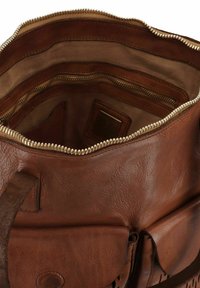 Intérieur d'un sac à main en cuir brun avec une fermeture éclair, plusieurs compartiments, des surfaces lisses et texturées, et une étiquette de marque.