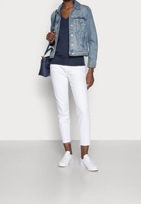 Chaqueta de mezclilla, top azul marino de escote en V, jeans blancos hasta los tobillos y zapatillas blancas. El atuendo está complementado con un pequeño bolso azul.