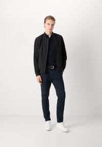Black bomber jacket, navy pants, white sneakers. Smooth fabric, tapered fit, zip front, elastic cuffs, and a simple belt detail.
