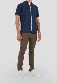Chemise bleu marine à manches courtes avec boutons et col, portée sur un tee-shirt blanc, assortie à un pantalon kaki slim et des baskets blanches.