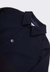 Cappotto di lana blu navy con colletto piegato e due bottoni visibili, esposto su uno sfondo grigio chiaro.