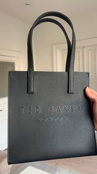 Sac tote noir texturé avec double poignée et logo embossé « TED BAKER LONDON » tenu par une main dans un cadre intérieur neutre.