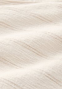 Primo piano di tessuto beige morbido con sottili righe orizzontali e superficie leggermente irregolare e strutturata.