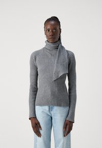 Sivi rebrasti pulover s turtleneck ovratnikom in dolgimi rokavi. Kombiniran z svetlo modrimi hlačami, ki imajo sproščen kroj.