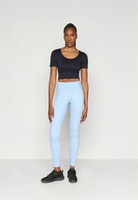 Top corto nero, leggings azzurri chiaro e scarpe sportive nere. Tessuto liscio, design aderente e vita alta sui leggings.