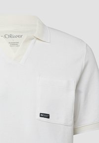 Biała polo z krótkim rękawem, posiadająca kołnierzyk, kieszeń na piersi oraz małą czarną metkę "Elevated Casual" na kieszeni.