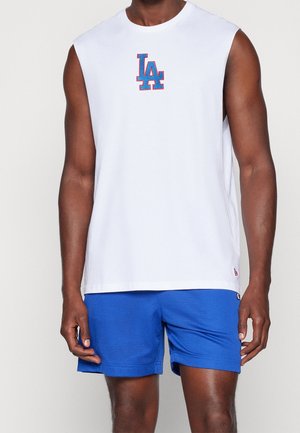 Uomo che indossa una canotta bianca con il logo "LA" blu e rosso e pantaloncini sportivi blu.