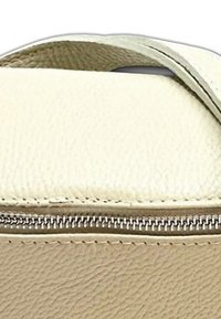 Crème-kleurige leren zak met een gladde textuur, voorzien van een metalen ritssluiting en een gebogen handvat bovenaan. De randen zijn netjes gestikt.