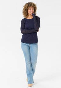 Navy long-sleeve top with knit mesh sleeves, paired with light blue flared jeans and beige footwear. Set against a plain white background.