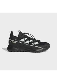 Černá trailová běžecká obuv Adidas Terrex se bílými pruhy, odrazivými detaily a elastickým šněrovacím systémem na světle šedém pozadí.
