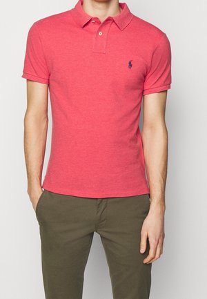 Polo rouge en coton avec une finition texturée. Il présente un col classique, des manches courtes et un petit logo brodé sur la poitrine.