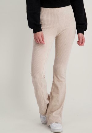 Beige corduroy flared broeken met verticale ribbelstructuur. Hoge taille design gecombineerd met witte sneakers.