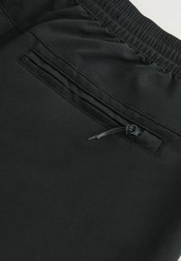 Pantaloni scurți negri dintr-un material neted, cu un elastic la talie și o buzunar la spate cu fermoar, dotat cu un tab de tragere.