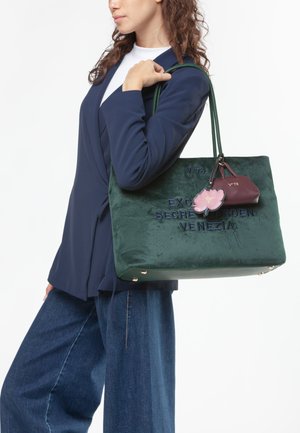 Borsa tote in velluto verde con testo ricamato "EXCELSIOR SECRET GARDEN VENEZIA," dotata di un charm floreale e una piccola pochette di accento borgogna.