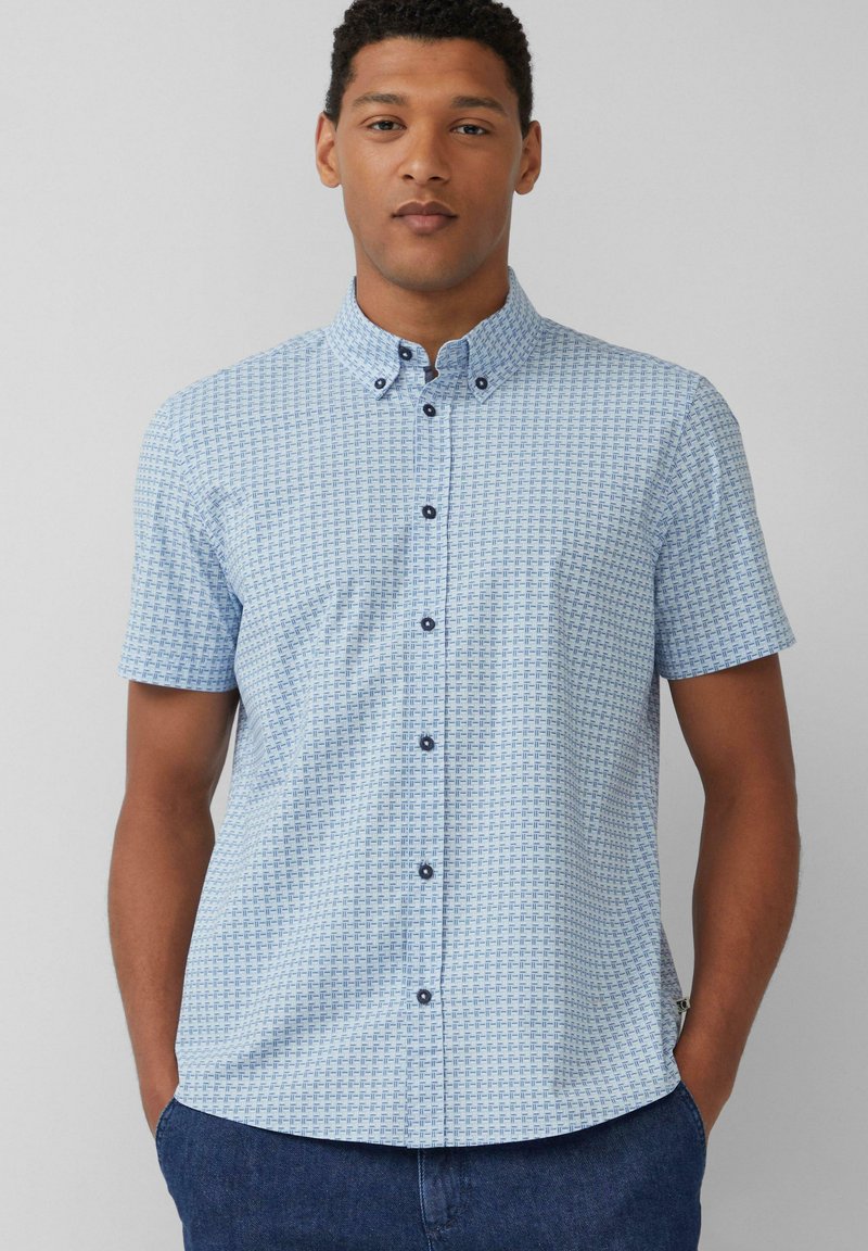 Chemise à manches courtes à boutons de couleur bleu clair avec un motif géométrique. Présente un col boutonné et des boutons navy. Tissu en coton lisse.